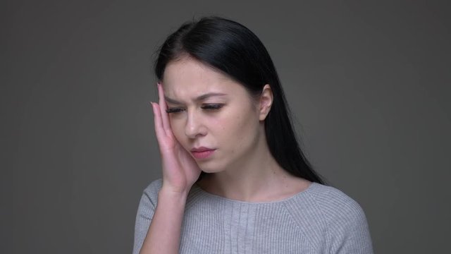 Closeup shoot of young pretty brunette caucasian female having a headache and being tired with background isolated on gray