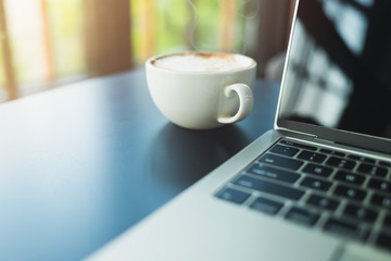 Latte coffee in a white coffee mug And laptop side On a black wooden table in the morning coffee shop