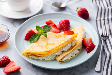 Crepes, thin pancakes with fresh strawberry and ricotta, cream cheese stuffing. Marble background.