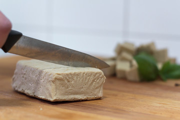 Woman with knife cutting tofu on wooden board