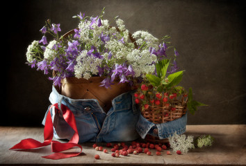Wild flowers in  basket set in jeans with  red ribbon and wild strawberries. Still life in vintage style.