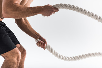 partial view of sportive man doing exercise with ropes on white background