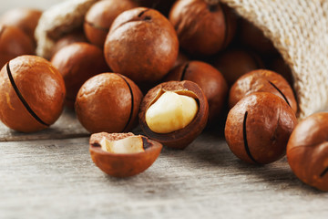 Macadamia nuts spilled out of the bag on a wooden background close-up with one peeled nut