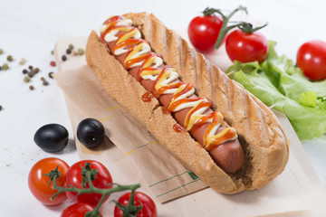 hot dog with sauces on served table with vegetables, olives and spices