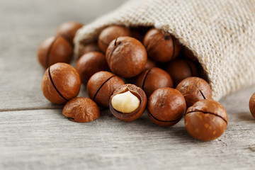Macadamia nuts spilled out of the bag on a wooden background close-up with one peeled nut