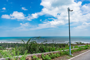 Close view of greenery shrub with sea beach & blue sky scenery from a top of a mountain road.