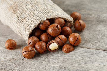 Macadamia nuts spilled out of the bag on a wooden background close-up with one peeled nut