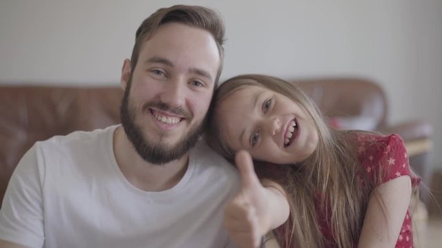 Portrait of handsome bearded man and cute positive girl looking in the camera smiling. The child leans her head to the man. Father and daughter having fun at home, leisure of the happy family