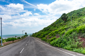 straight road going to downwards down of a mountain with blue ocean & blue sky background. 