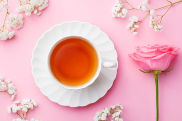 Cup of tea with fresh flowers on pink background. Copy space. Top view.