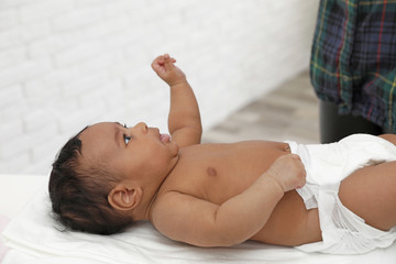 Cute African-American baby lying on scales indoors