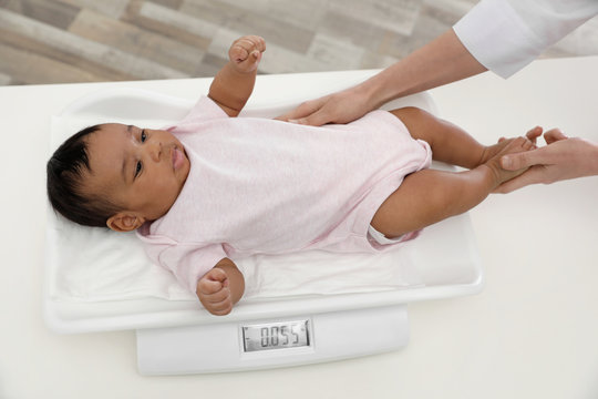 Doctor weighting African-American baby on scales indoors, above view