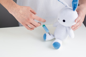 Kids medicine concept. Cute and friendly poster representing children healthcare. Nurse making an injection with syringe to toy bunny.