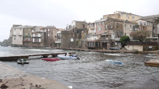 Erbalunga, Corsica, France - april 22 2019: Large waves batter on the harbor of Erbalunga (fishing village) with the boats crushing into the dock. The stormy sea on (tower) Torra d'Erbalunga