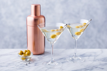 Martini cocktail with green olives, shaker on marble table background. Copy space.