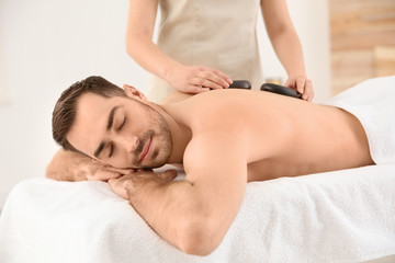 Fototapeta na wymiar Handsome man receiving hot stone massage in spa salon