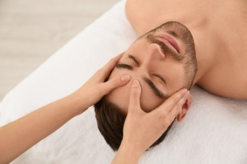 Fototapeta na wymiar Handsome man receiving face massage in spa salon