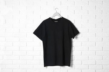 Hanger with black t-shirt against brick wall. Mockup for design