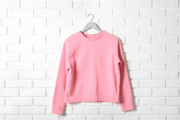 Hanger with pink sweatshirt against brick wall. Mockup for design
