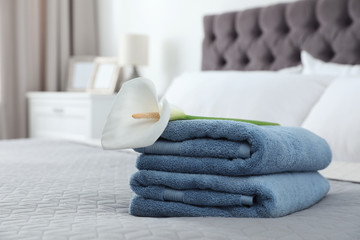 Fototapeta na wymiar Stack of clean towels with flower on bed indoors