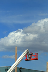 Cherry picker crane and hydraulic construction cradle with white clouds and blue sky on background