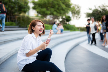 Young beautiful Asian lady celebrate with smart phone in the street in a sunny summer day, success happy pose, internet technology.