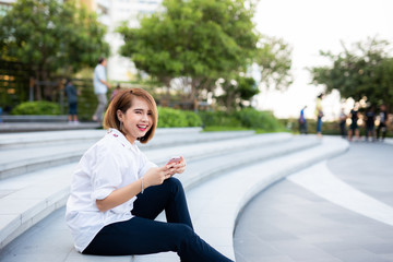 Young beautiful Asian lady celebrate with smart phone in the street in a sunny summer day, success happy pose, internet technology.