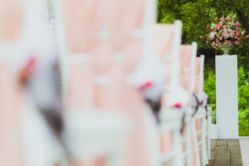 Beautiful setting for outdoors wedding ceremony. Chairs for guests of the bride and groom are decorated in the same style, decorated with fashionable fabric.  chairs are placed convolution with  rose 