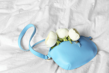 Stylish bump bag with spring flowers on crumpled white sheet