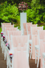 Beautiful setting for outdoors wedding ceremony. Chairs for guests of the bride and groom are decorated in the same style, decorated with fashionable fabric.  chairs are placed convolution with  rose 