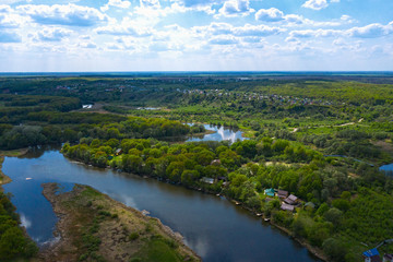 Fototapeta na wymiar Aerial view of river with reflected blue sky and clouds, green meadows with trees and plants. Beautiful summer nature landscape from above