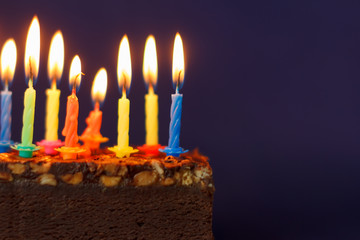 Happy Birthday Brownie Cake with Peanuts, Salted Caramel and Colorful Burning Candles on the Violet Background. Copy Space for Text.