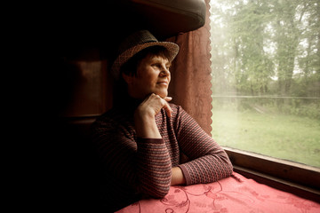 Portrait of beautiful 60 years old woman in hat sitting in train