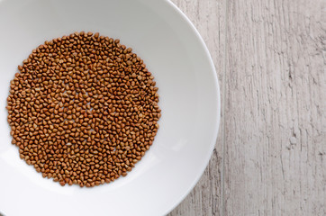 Dry raw buckwheat in white ceramic dish on wooden background.
