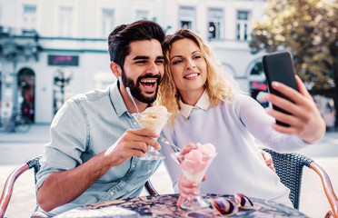 Dating in the cafe. Loving couple eating ice cream and taking a selfie with a mobile phone. Love and relationships