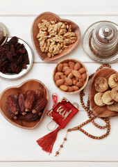 Ramadan iftar party concept. Islamic holy book Quran and rosary beads with delicious dates, dried figs, dried apricots, walnuts, almonds, raisins on bamboo plates on a white wooden table background.