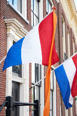 Dutch flags with orange streamer waving in the wind on facades of typical dutch houses on Koningsdag in the Netherlands. A national holiday in the Kingdom of the Netherlands. Vertical image