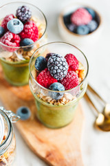 Top view on portions of chia pudding with matcha tea, organic granola, frozen berries in glasses. The concept of healthy vegan food.