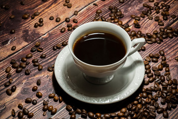 Cup of coffee surrounded by coffee beans  on wooden table.