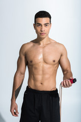 handsome mixed race man with muscular torso holding jump rope and looking at camera on white