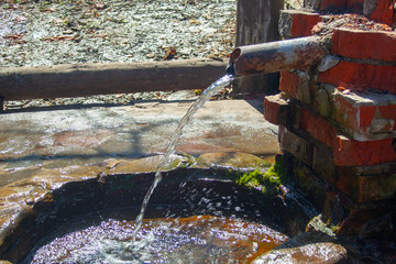 Natural spring folded of old bricks and metallic pipe. Clean fresh nature water source from the...