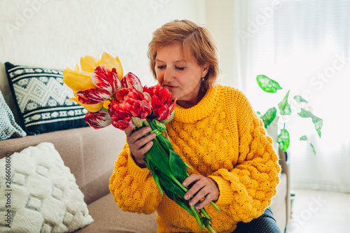 Senior woman smelling bouquet of tulips from her kids at home. Mother's day present