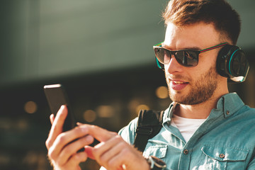 Young man listening to music via headphones and smartphone on the street