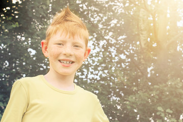 smiling red-haired boy looks at the camera with positive emotions in the park on a summer day,...