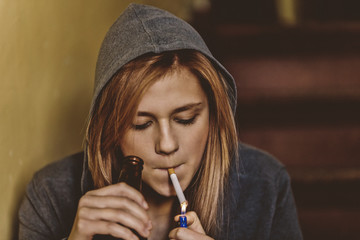Teenage girl is holding cigarette and bottle with beer. Illegal adolescent problem.