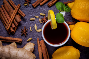 Concept of the winter warming drink. Lemon, tea, spices, ginger, cinnamon on a black stone background