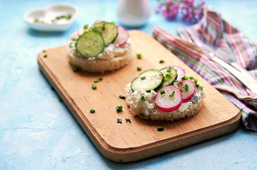 White bread sandwiches with salted cottage cheese, fresh radish and cucumber on a light blue background. Healthy food.