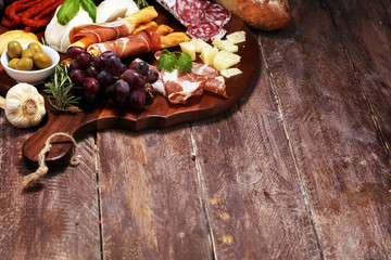 antipasto various appetizer. Cutting board with prosciutto, salami, cheese, bread and olives on dark wooden background
