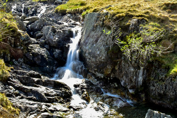 Naklejka na ściany i meble Stream leading out to small waterfall. Slow shutter speed. Bright sunny day. Grisedale pike, Lake District, England, UK