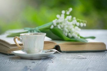 A cup of hot coffee, a bouquet of lilies of the valley, the old book